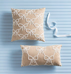 Two beige pillows with white bow patterns on a light blue wooden background