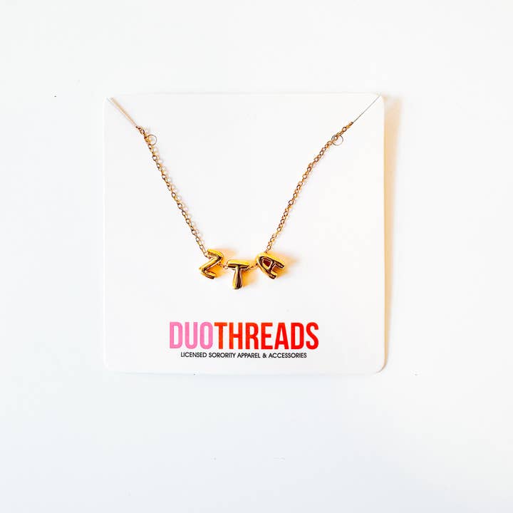 A gold chain necklace with a  'ZTA' pendant, displayed on a white card with the brand name 'DUOTHREADS' printed in pink and red.