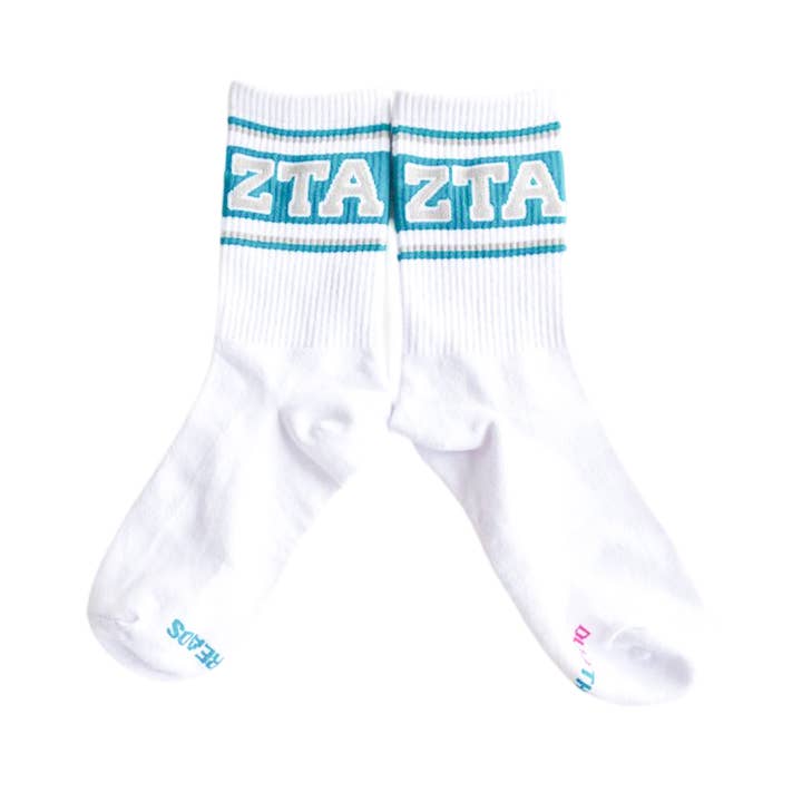 A pair of white crew socks with a bold turquoise and white 'ZTA' logo across the ribbed cuffs, displayed against a clean white background.
