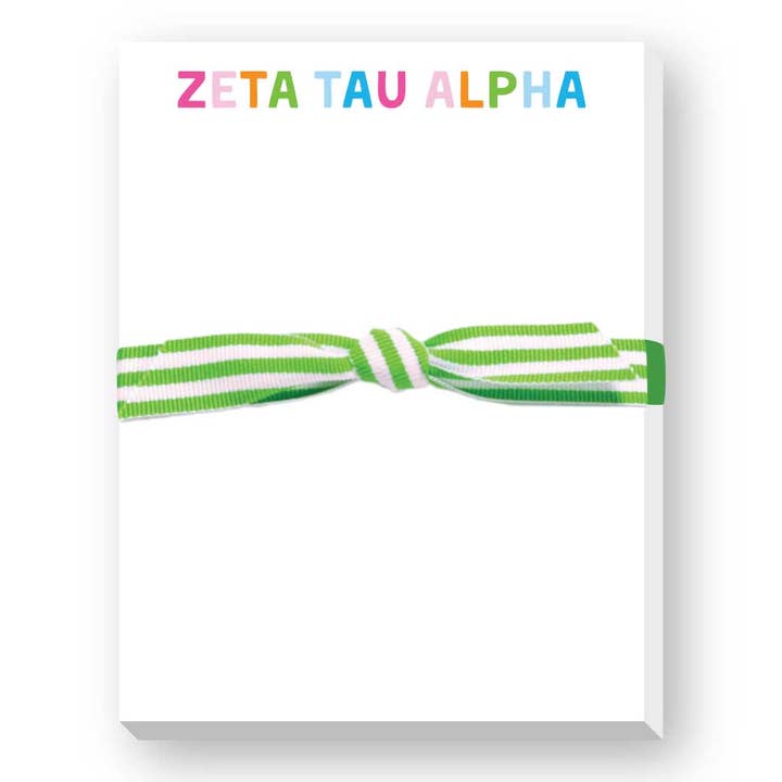 A white rectangular notepad or card with the words 'ZETA TAU ALPHA' printed at the top in multicolored letters, tied across the center with a green and white striped ribbon.