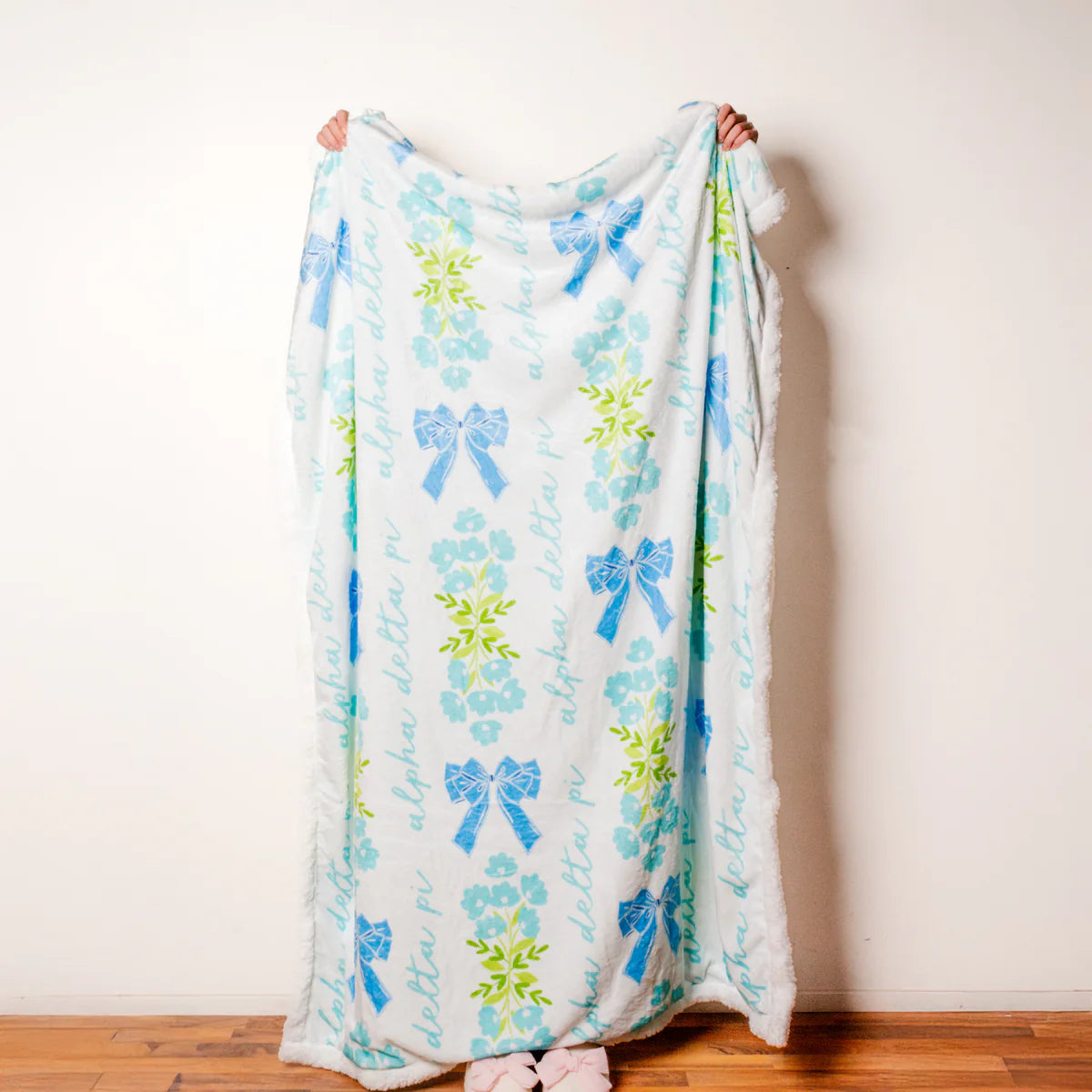 Person holding a decorative blanket with blue bows and floral patterns on a plain background