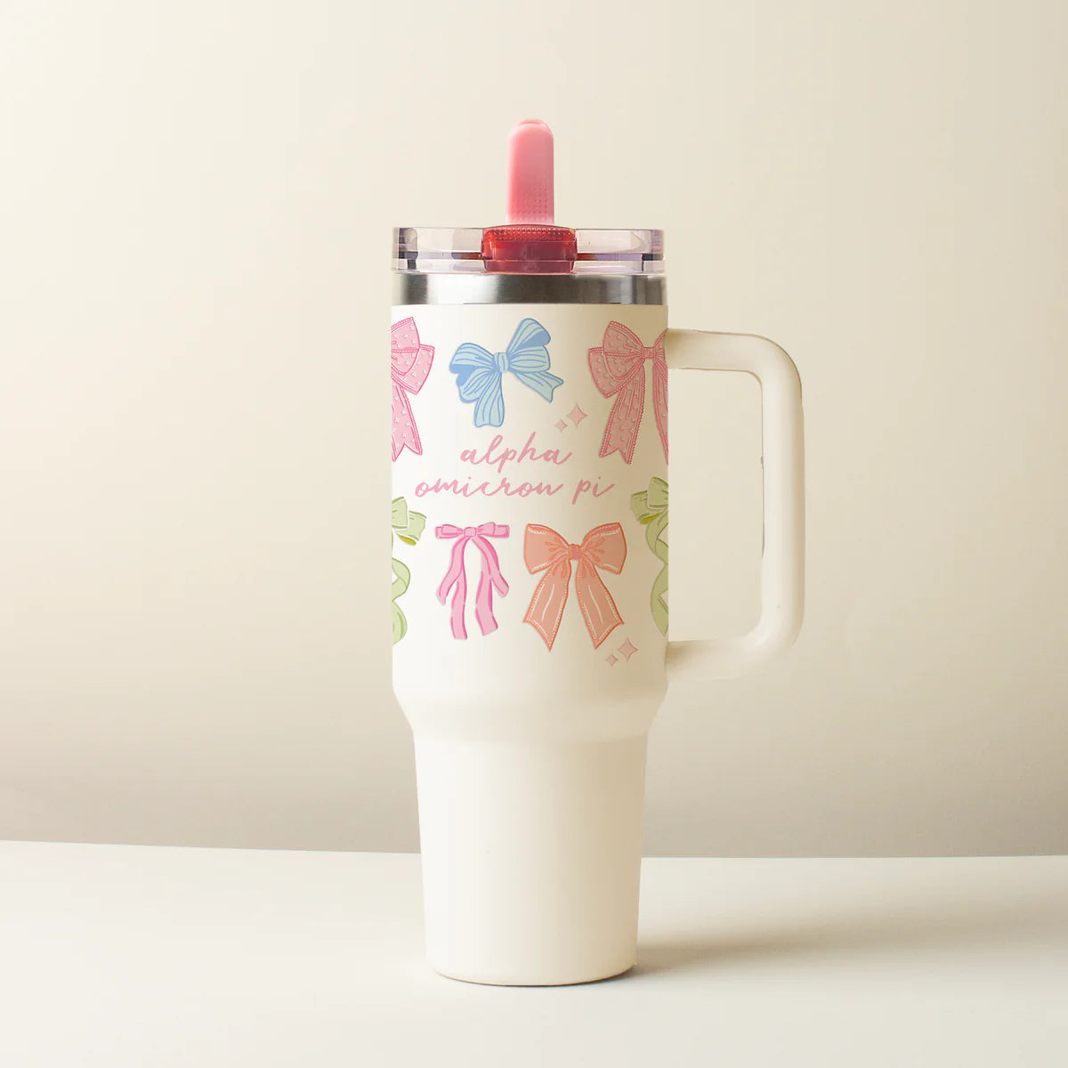 Tumbler with colorful bow designs on a beige background saying Alpha Omicron Pi