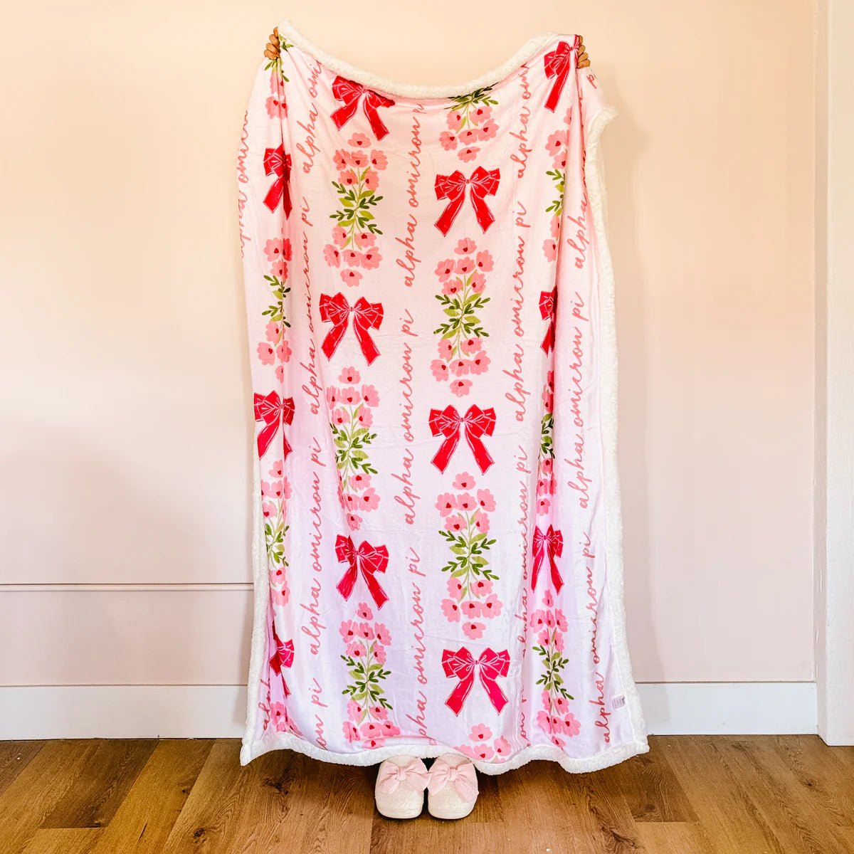 Person holding a decorative blanket with red bows and floral patterns on a plain background
