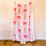 Person holding a decorative blanket with red bows and floral patterns on a plain background