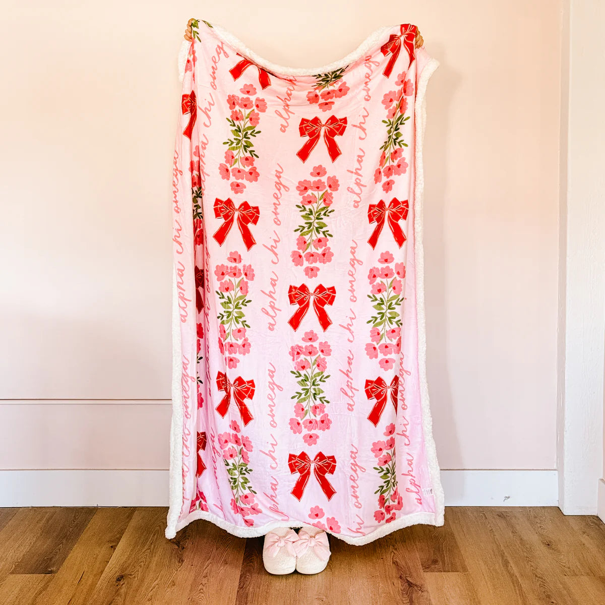 Person holding a decorative blanket with red bows and floral patterns on a plain background