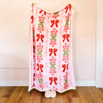 Person holding a decorative blanket with red bows and floral patterns on a plain background