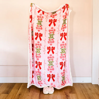Person holding a decorative blanket with red bows and floral patterns on a plain background