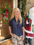 Woman modeling a dark denim blouse with short bubble sleeves and a v-neck collar in front of a door with Christmas decorations, including a wreath and Santa figure.