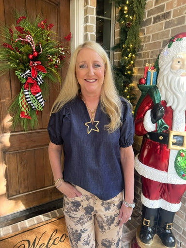Woman modeling a dark denim blouse with short bubble sleeves and a v-neck collar in front of a door with Christmas decorations, including a wreath and Santa figure.