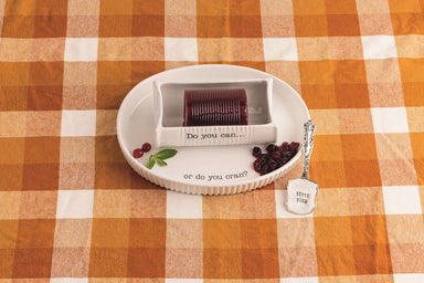 White ceramic cranberry serving dish sitting on an orange and white checkered tablecloth featuring a well to hold homemade cranberry sauce and attached center well to hold the canned version. Comes with stamped silverplate spatula. 