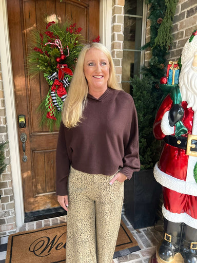 Woman wearing a chocolate brown long sleeve sweater with tan cheetah print pants standing in front of a door with Christmas decorations