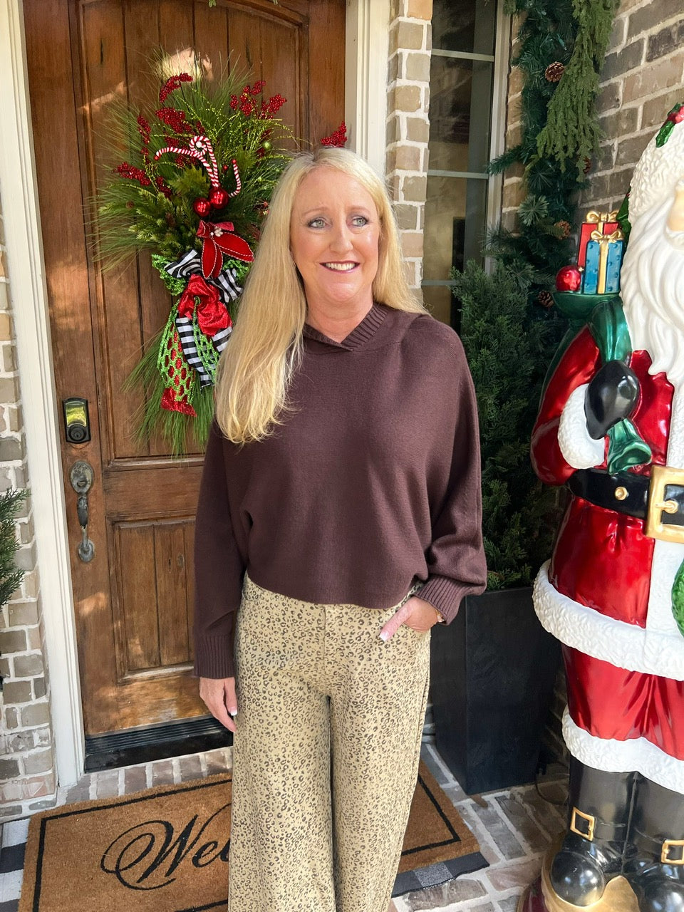 Woman wearing a chocolate brown long sleeve sweater with tan cheetah print pants standing in front of a door with Christmas decorations