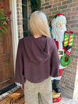 Woman modeling the back a chocolate brown long sleeve hooded sweater with tan cheetah print pants standing in front of a door with Christmas decorations