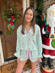 Woman in festive pajama set standing next to a decorated door with wreath and Santa Claus figure.