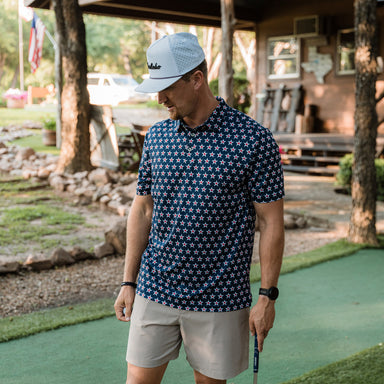 Man in a star-patterned shirt and cap standing on a putting green.