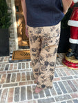 Woman modeling beige floral pants standing on a brick porch with a 'Welcome' mat.