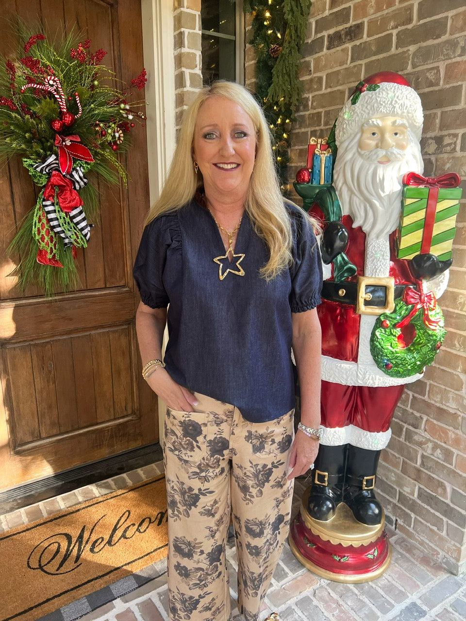 Person wearing beige floral pants standing on a brick porch with a 'Welcome' mat.