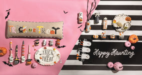 Halloween-themed decor items including a pillow, candles, and a sign on a pink and black striped background.