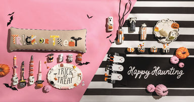 Halloween-themed decor items including a pillow, candles, and a sign on a pink and black striped background.