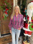 Woman wearing a pink and green plaid shirt with jeans embellished with pearls next to a Santa Claus statue in front of a door with Christmas decorations.