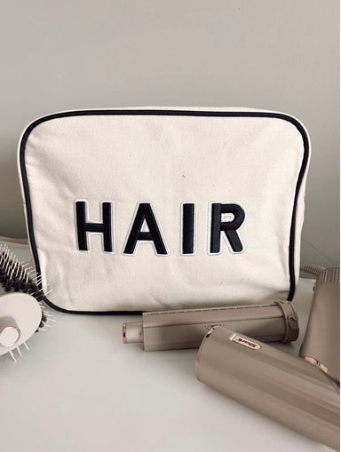 Photo of an XL light beige canvas accessory or makeup bag with a black trim and black patch letters saying Hair sewn on the front 