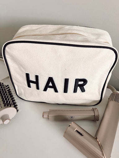 Photo of an XL light beige canvas accessory or makeup bag with a black trim and black patch letters saying Hair sewn on the front