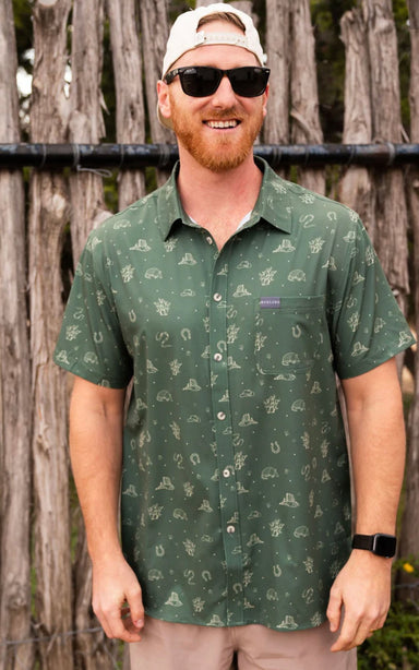 Man modeling our forest green button up shirt with a pattern of armadillos, cacti, hats, horseshoes, and snakes. 
