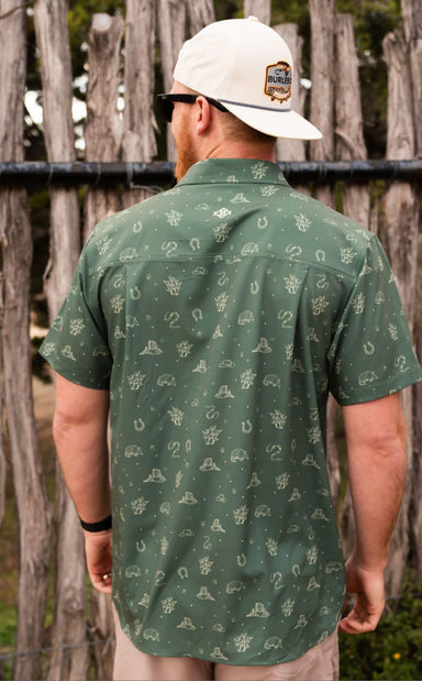 Man modeling the back of our forest green button up shirt with a pattern of armadillos, cacti, hats, horseshoes, and snakes.