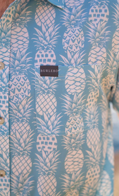 Up close photo of the pineapple print and chest pocket our light blue, short sleeve button up shirt 