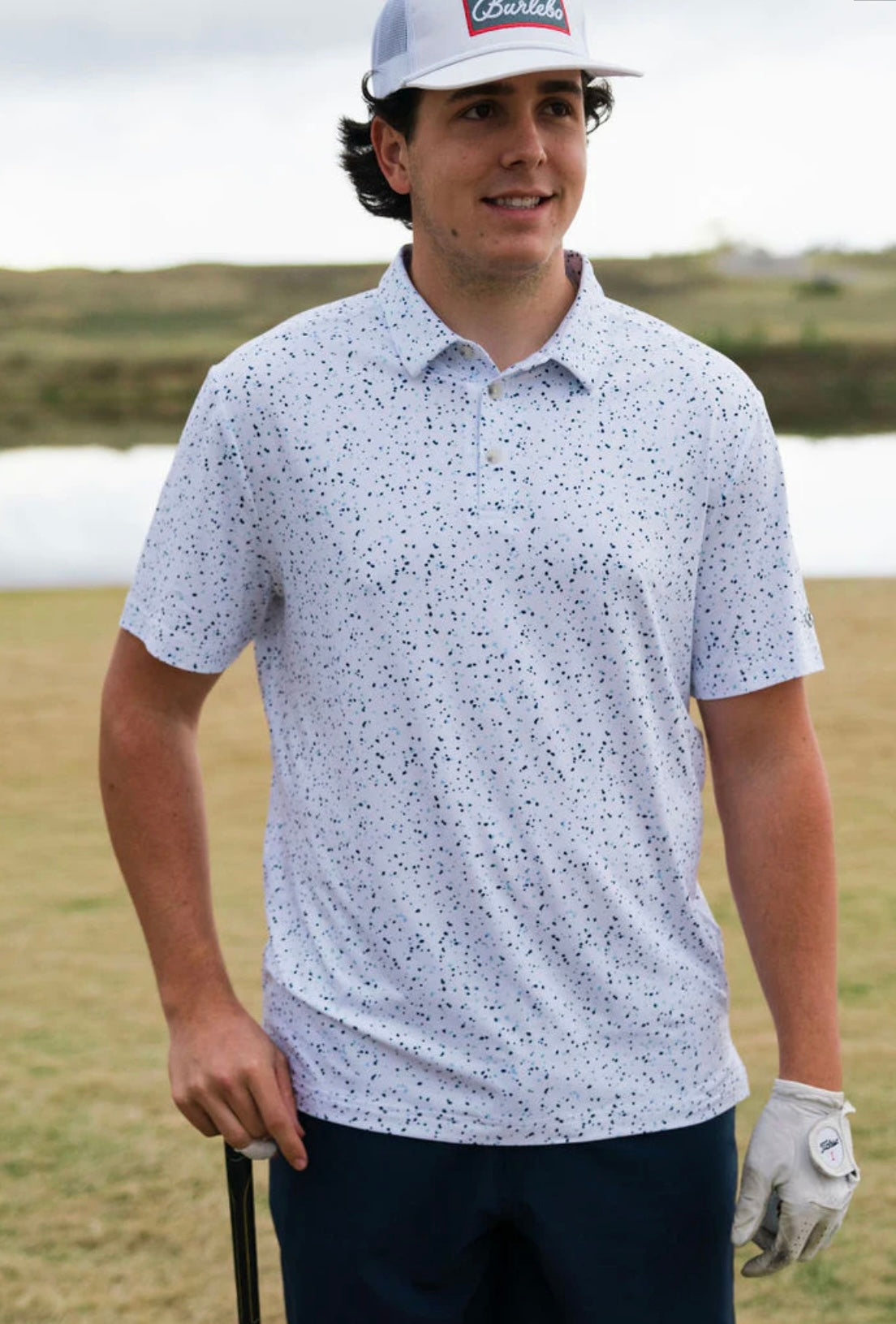 A man modeling the front of this white performance polo with a blue speckled pattern all over