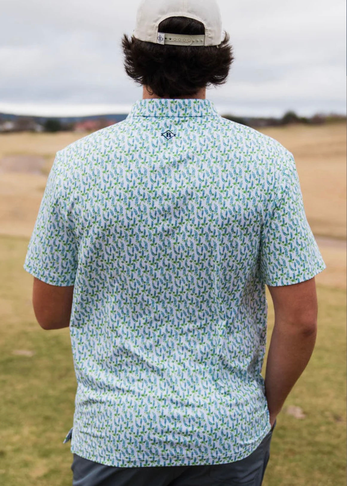 Man modeling the back of our white, short sleeve, performance polo with little bluebonnets all over