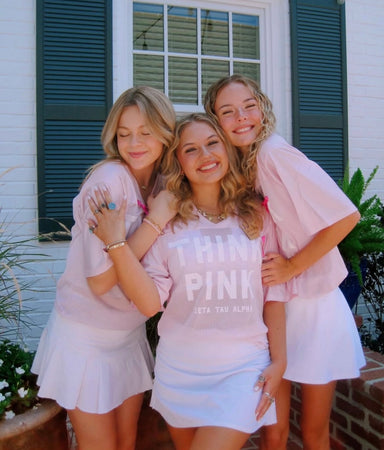 Three women in matching pink and white outfits posing together outdoors.