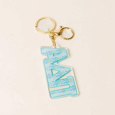 A Greek letter keychain featuring the letters 'ΑDPi' in light blue with a floral pattern, attached to a gold-tone lobster clasp and split ring, set against a light cream background.