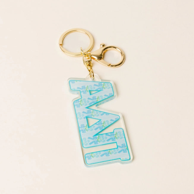 A Greek letter keychain featuring the letters 'ΑDPi' in light blue with a floral pattern, attached to a gold-tone lobster clasp and split ring, set against a light cream background.