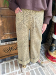 Up close photo of a person wearing leopard print pants standing on a brick sidewalk with a wooden door and doormat in the background.