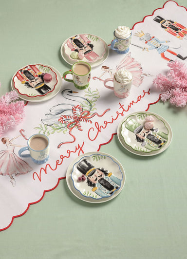 Table setting with Christmas-themed plates, mugs, and a decorative, Nutcracker-themed tablecloth.