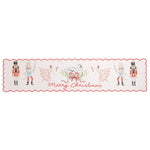 A rectangular holiday table runner with a scalloped red border, featuring watercolor illustrations of nutcrackers, ballerinas, a swan, candy canes, and the text 'Merry Christmas' on a white background.