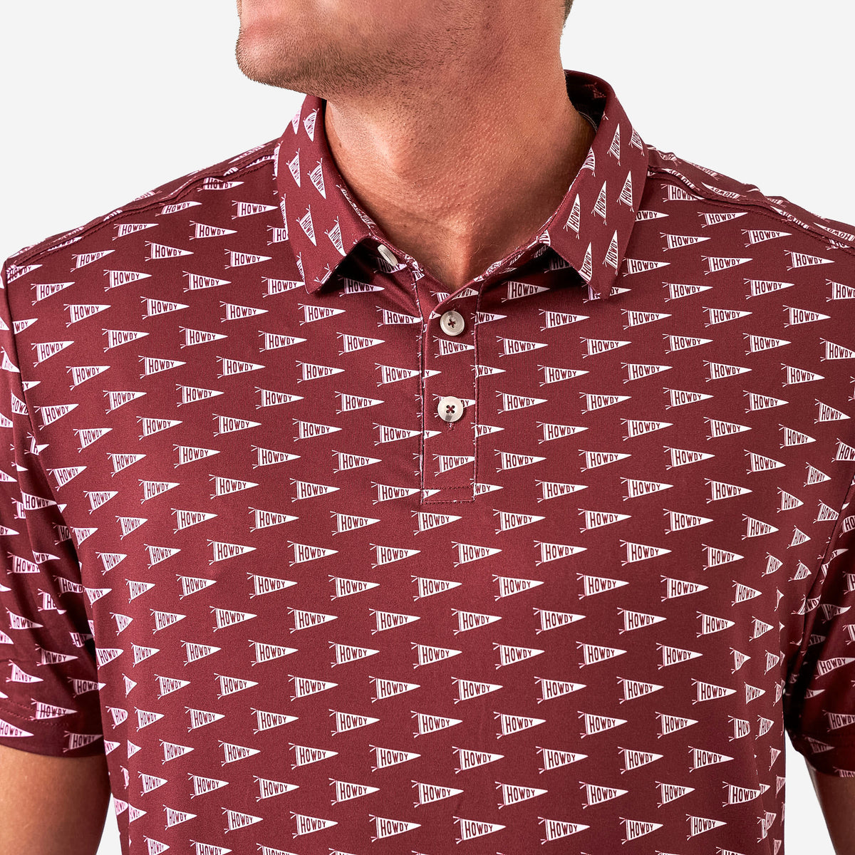 Up close photo of a maroon short sleeve polo with white pennants saying Howdy against a white background