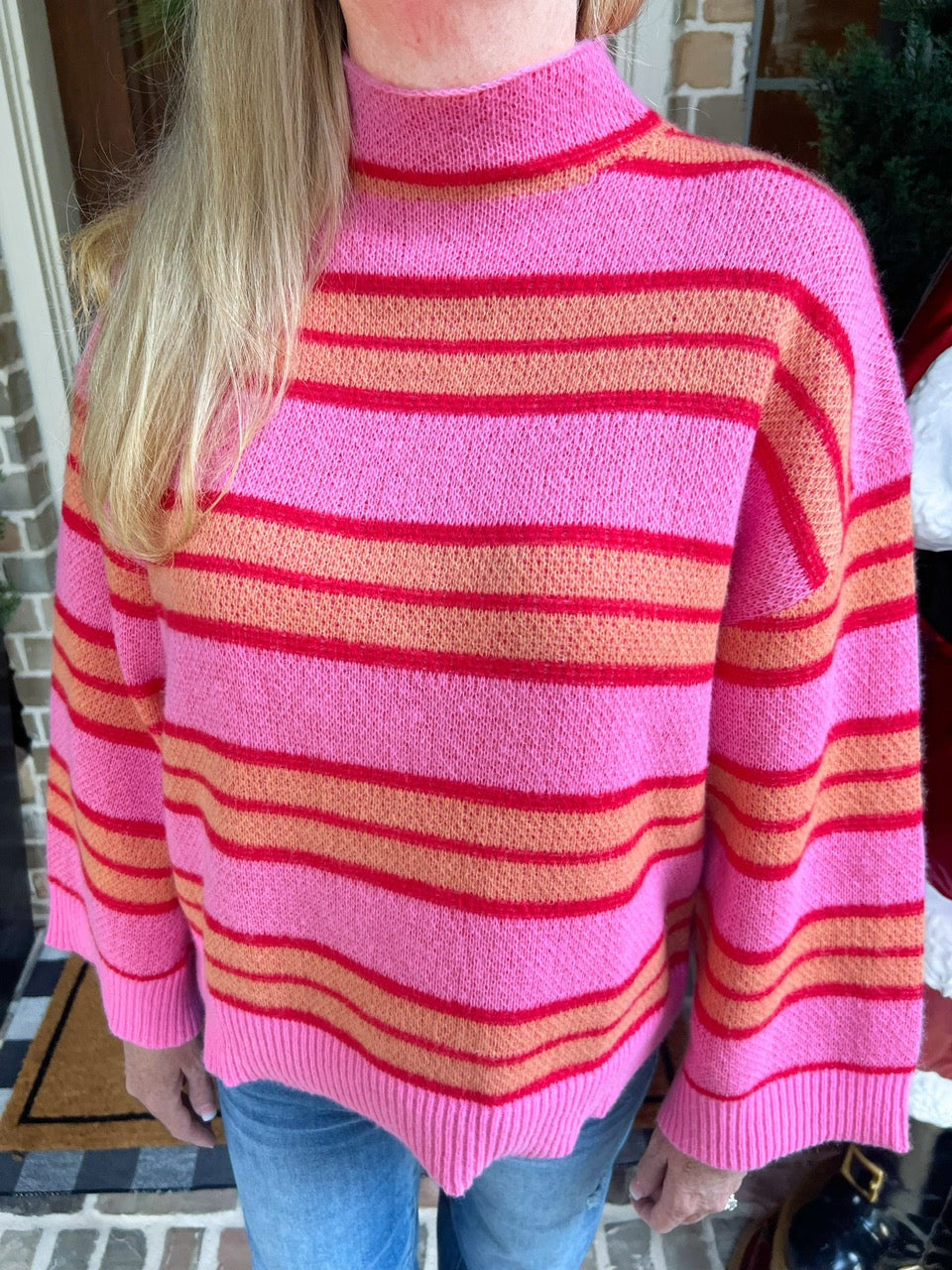 Person wearing a pink sweater with orange and red stripes with a blurred background
