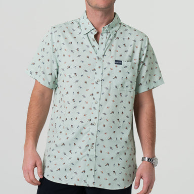 A man wearing a short-sleeved button-up shirt with a pattern of different fishing lures in a light color.