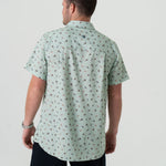 A man modeling the back of a short-sleeved button-up shirt with a pattern of different fishing lures in a light color.