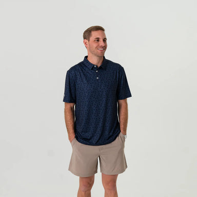 Another man modeling a full length photo a navy short sleeve polo with the American flag in shades of navy in an all over pattern.