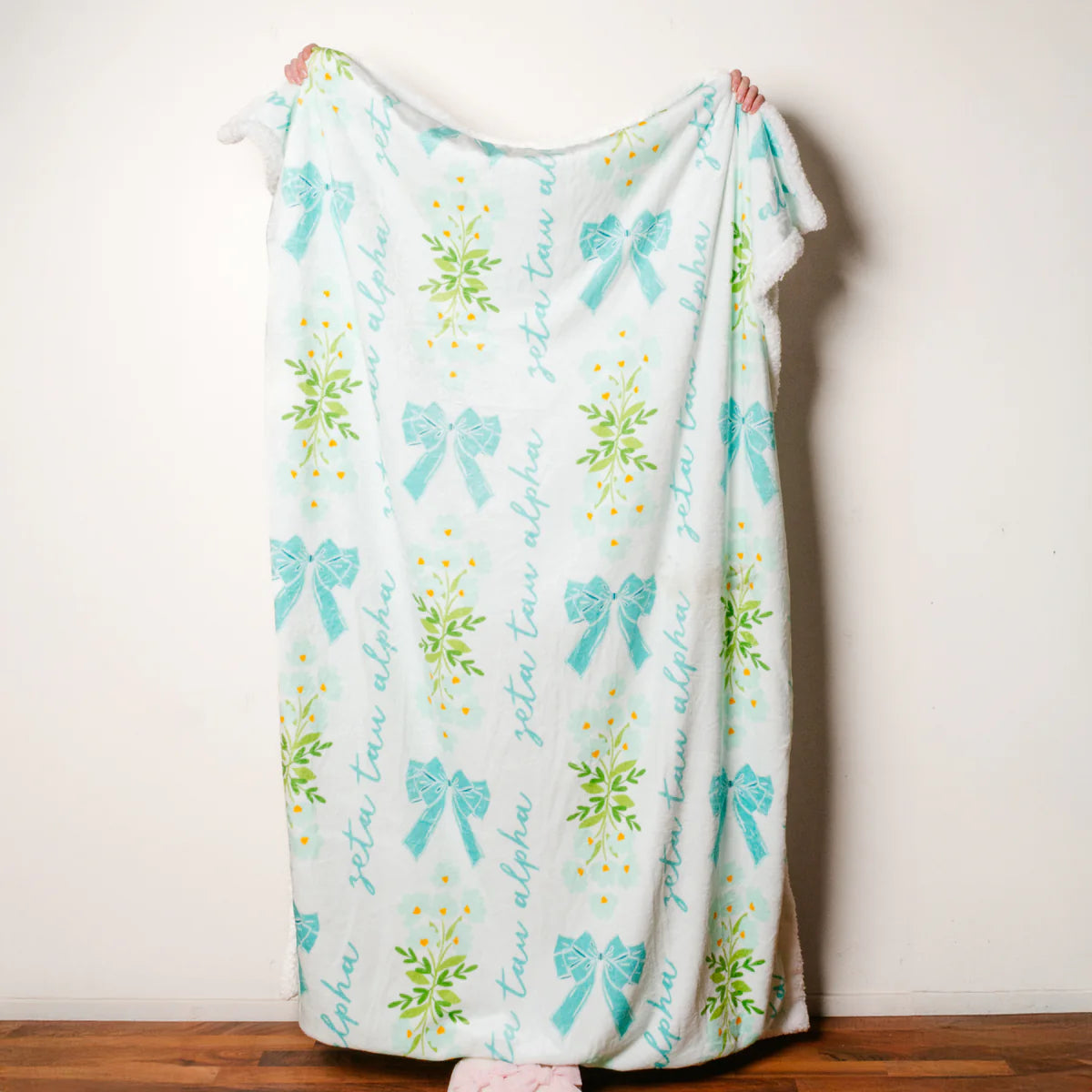 Person holding a decorative blanket with turquoise bows and floral patterns on a plain background