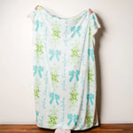 Person holding a decorative blanket with turquoise bows and floral patterns on a plain background