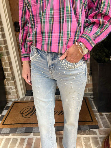 Woman wearing a pink and green plaid shirt with jeans embellished with pearls standing on a doormat.