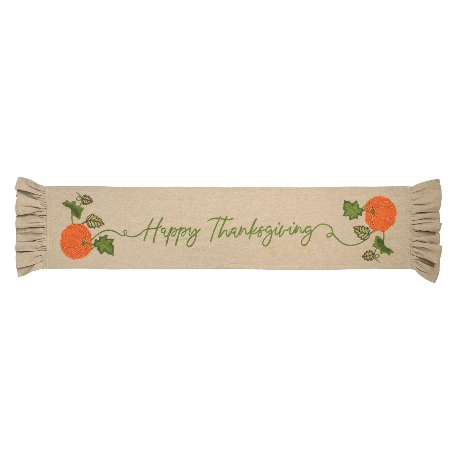 A beige fabric table runner with 'Happy Thanksgiving' embroidered in green script, decorated with orange pumpkins, green leaves, and pinecones on both ends, finished with ruffled edges.