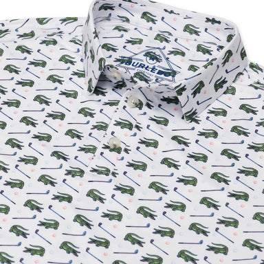 Up close photo of a white short sleeve polo with green alligators and golf clubs in an all over pattern